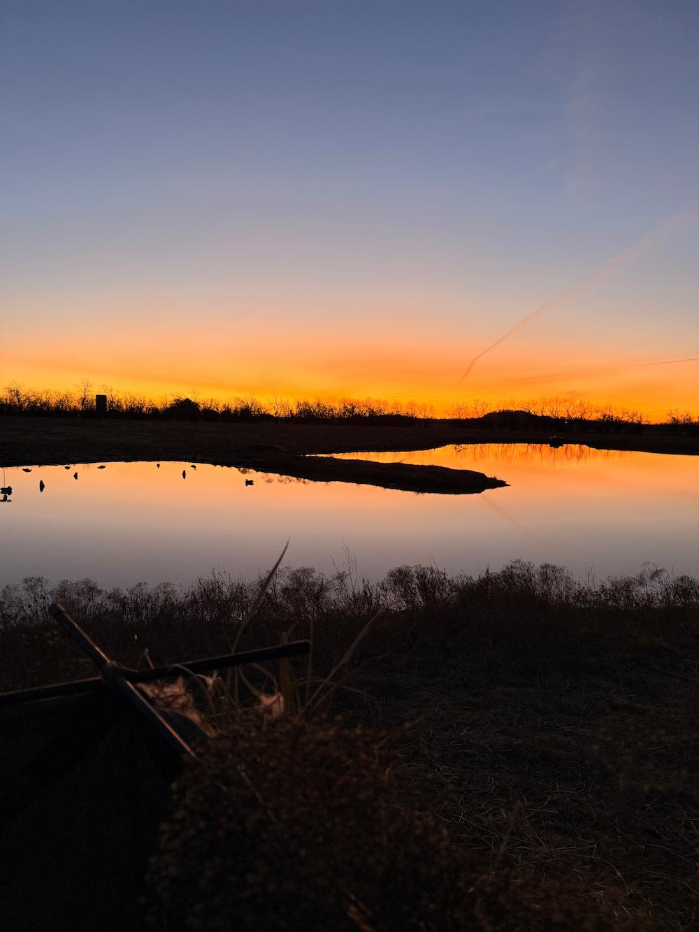 A scenic landscape photograph of a sunset over a calm lake, with a gradient sky transitioning from deep blue to vibrant orange and yellow, reflecting on the water's surface.